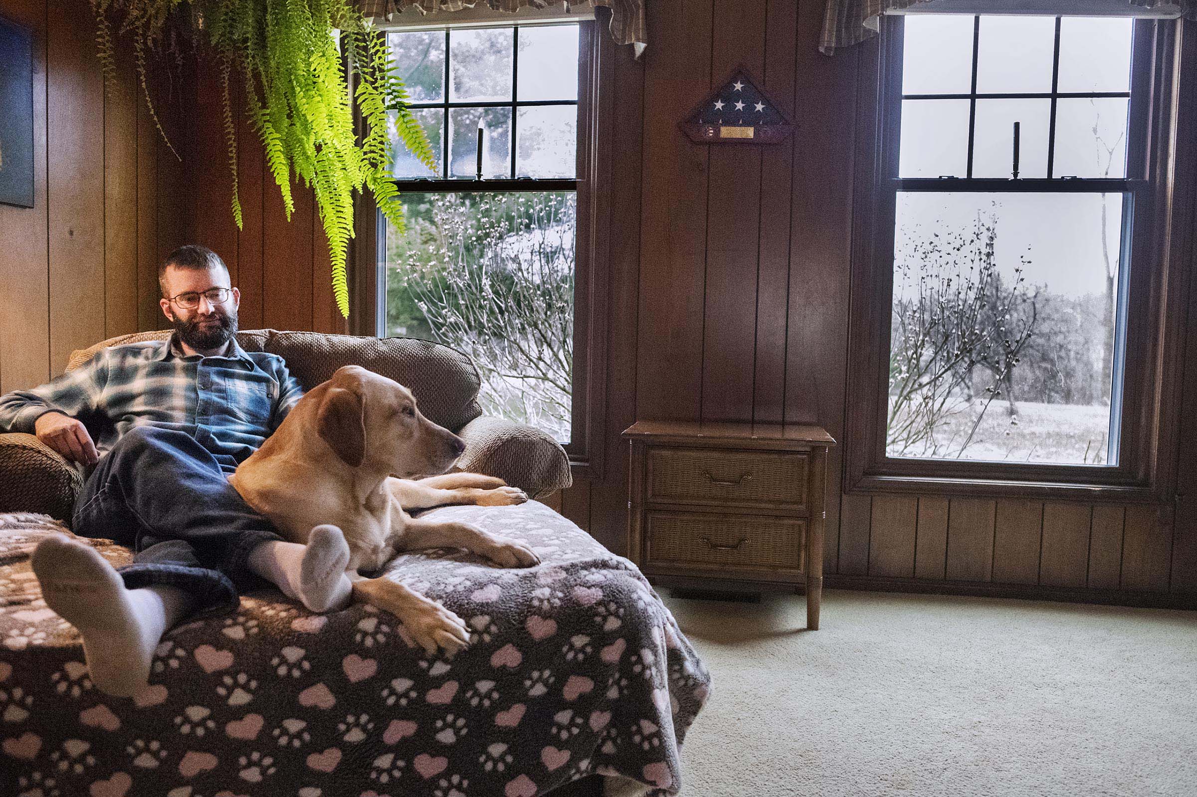    Adam sits on the couch with his mom's dog, Sunny. Adam finds comfort in her presence and when he was first back from deployment found it difficult to connect with people, but easier to connect with dogs.