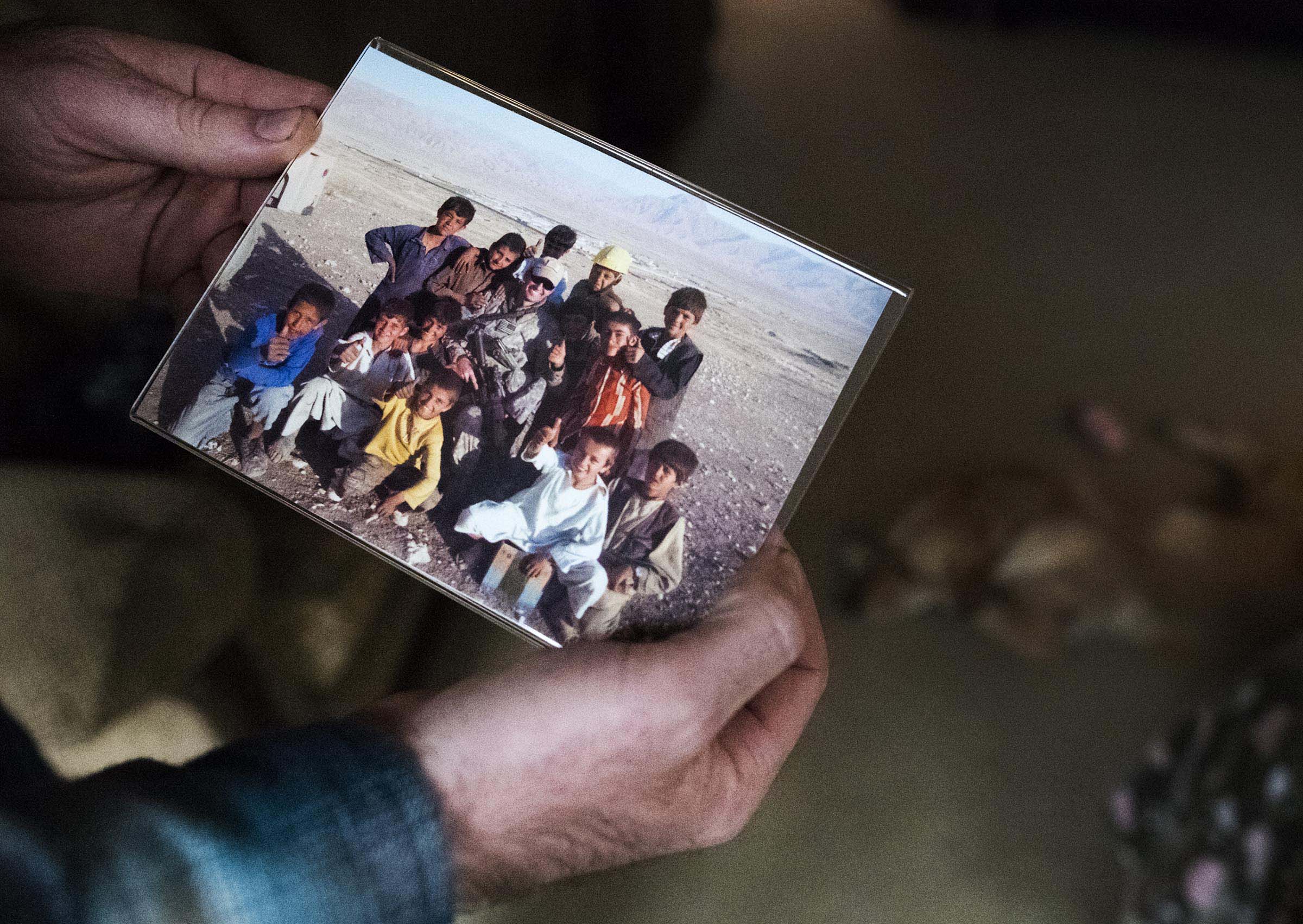 Adam holds his favorite photograph from his time in Afghanistan. In the photograph Adam is surrounded by local children, who he really felt connected to during his deployment.