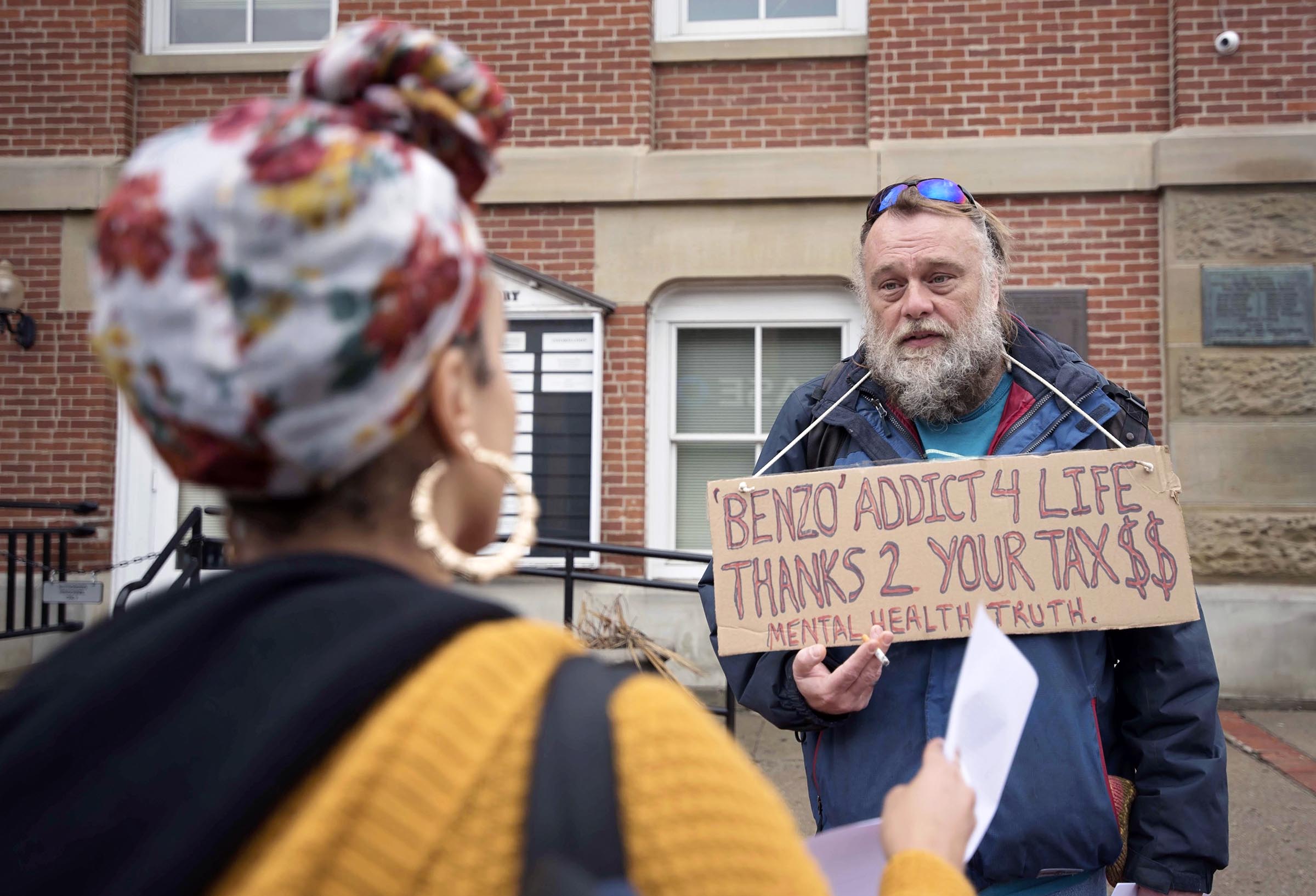    Pete Wuscher hands a copy of his medication dependency and human rights Manifesto to Ohio University student Myriah Smedley outside of the Athens County Courthouse.